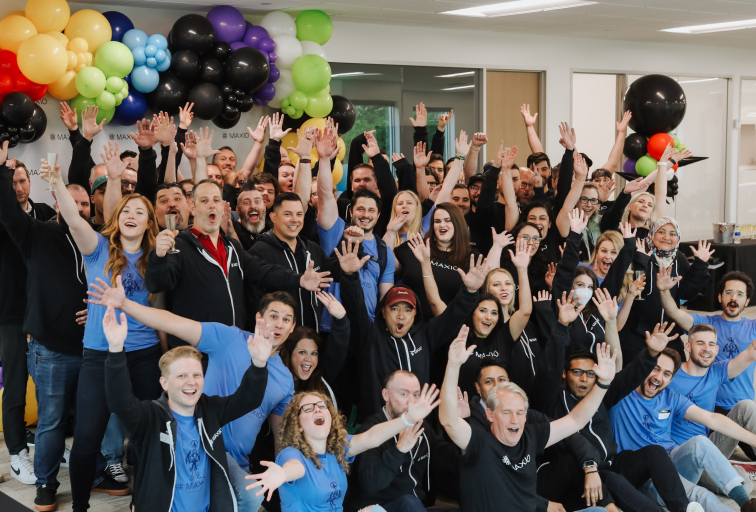 Photo of the Maxio team celebrating with their arms up and balloons in the background