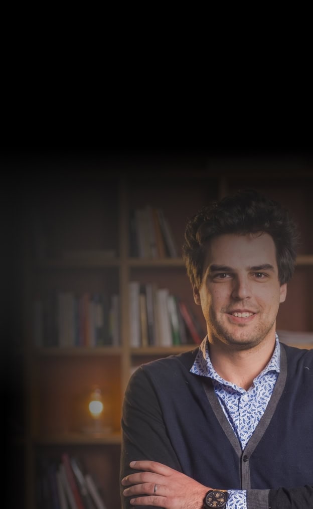 Young man smiling in a home office with bookshelves in the background.