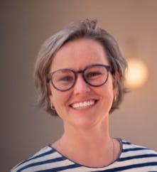 Smiling woman with glasses, short gray hair, wearing a striped shirt.
