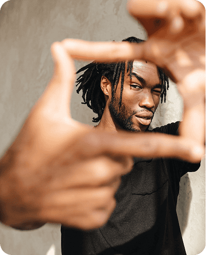 Portrait of a man with dreadlocks framing his face, looking through a frame made by hands.