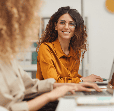 Smiling woman with glasses working on a laptop in an office setting.