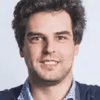 Portrait of a smiling man with curly hair and blue shirt for Maxio SEO.