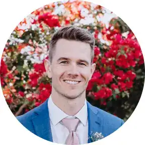 Professional man in a blue suit smiling outdoors with vibrant red flowers.