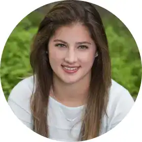 Young woman smiling outdoors with greenery in the background.