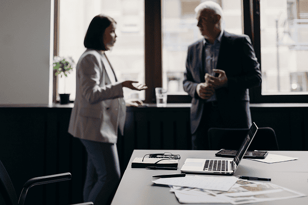 Business professionals discussing in a modern office with laptops and documents.